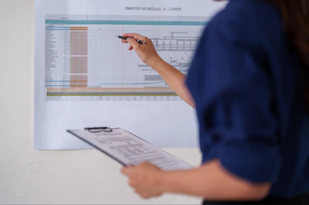 A project manager checking a detailed construction schedule with a pen and clipboard